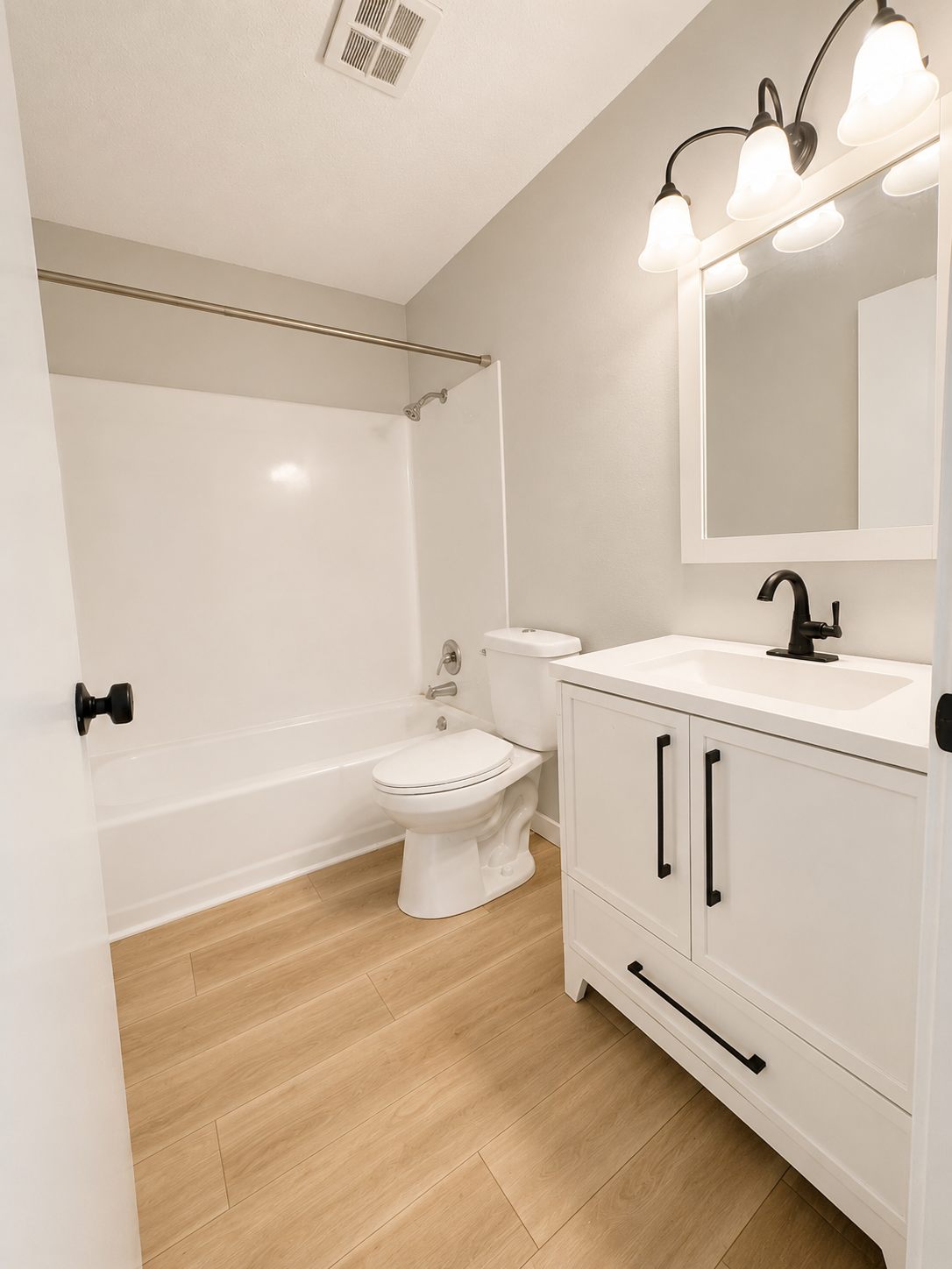 Renovated bathroom with white vanity, matte-black fixtures, framed mirror, and tub shower