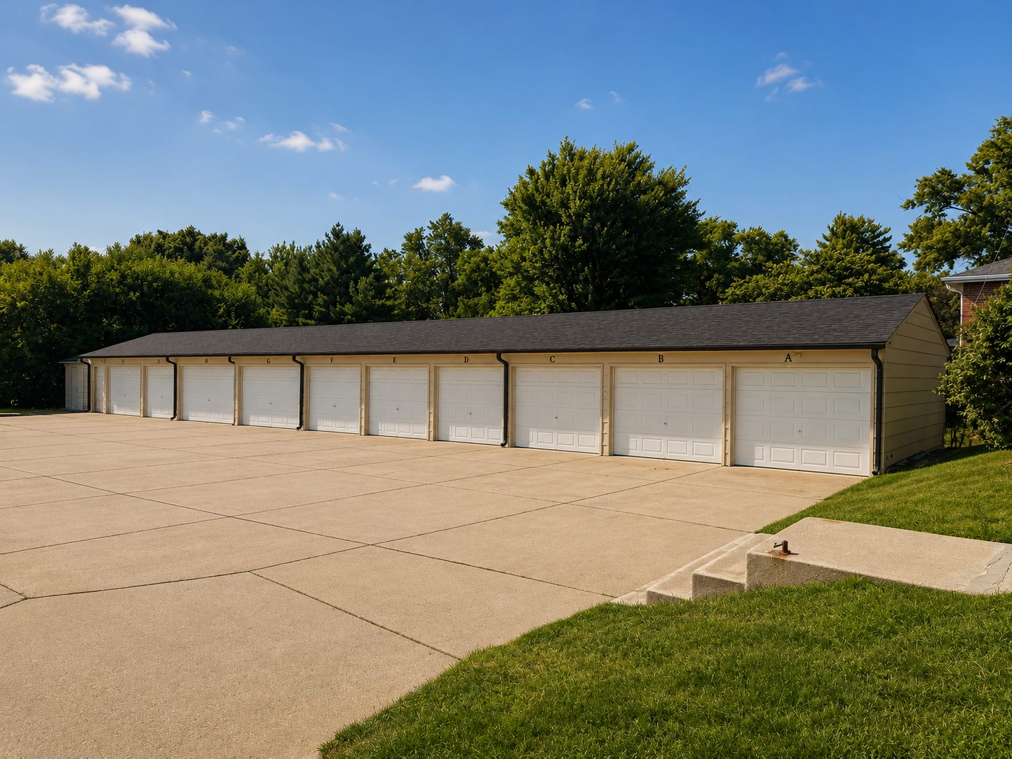 Row of private garage stalls with white doors, each lettered by residence, behind a wide concrete parking apron