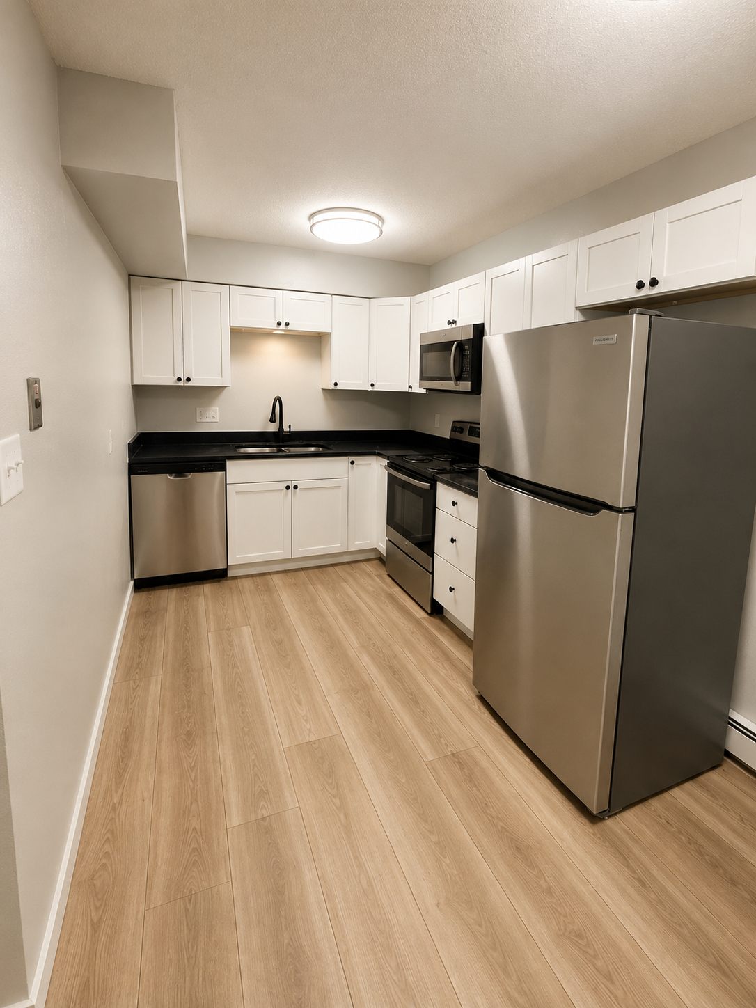 Renovated kitchen with white shaker cabinets, dark countertops, and the stainless suite — refrigerator, range, microwave, and dishwasher