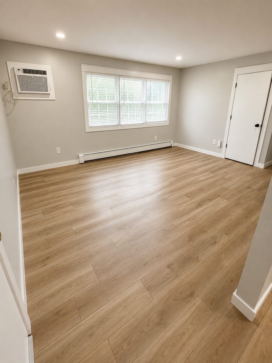 Renovated living room with new wide-plank flooring, recessed lighting, and a triple window